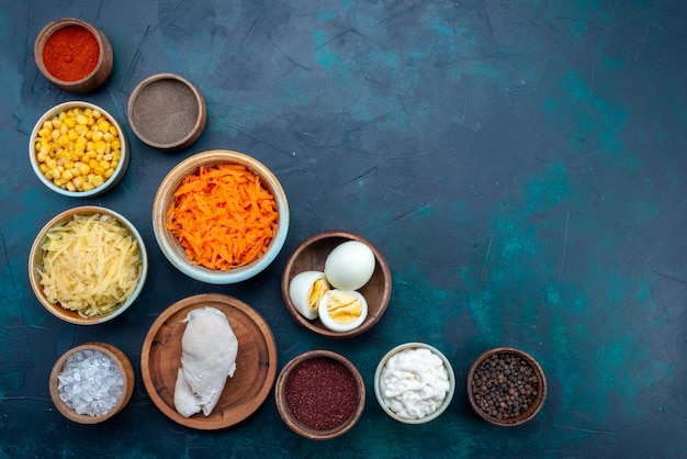 Top view different seasonings with eggs sliced carrots and cheese on dark blue background.