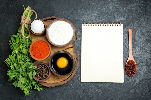 Top view different seasonings with flour notepad and egg on the grey space