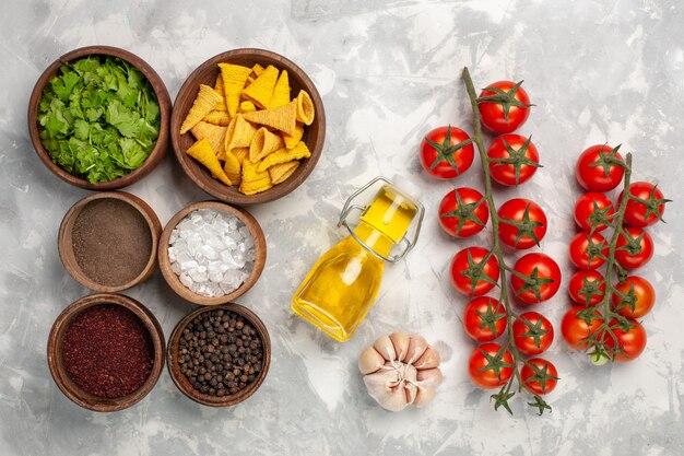 Top view different seasonings with greens and oil on the white desk