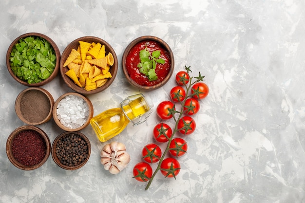 Top view different seasonings with greens tomatoes and oil on white desk