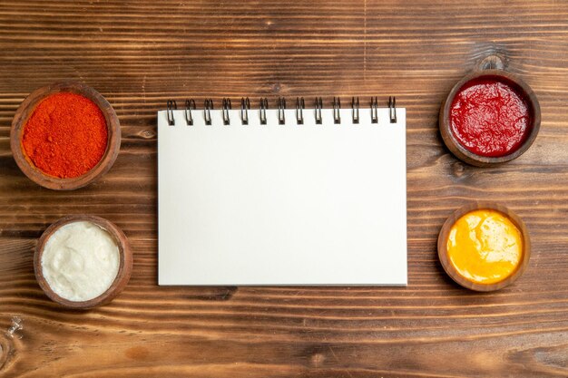 Top view of different seasonings with notepad on brown wooden table spicy ketchup tomato wood