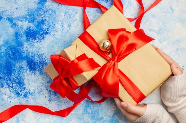 Top view different sizes gifts tied with red ribbon in woman hand on blue white table