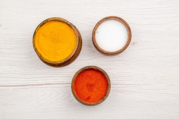 Top view different spices turmeric red pepper powder salt in small wooden bowl on grey background