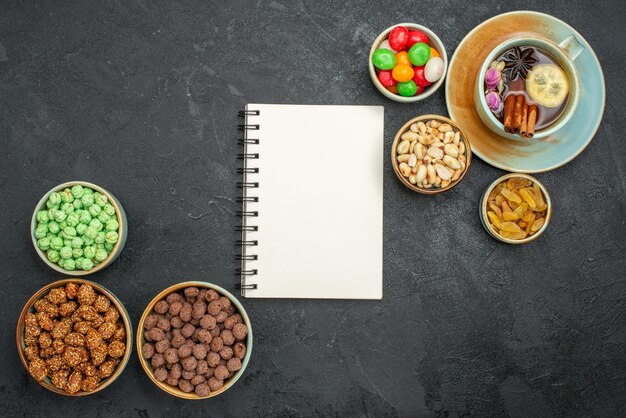 Top view of different sweet candies with cup of tea on grey