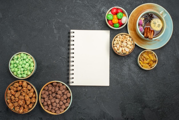 Top view of different sweet candies with cup of tea on grey