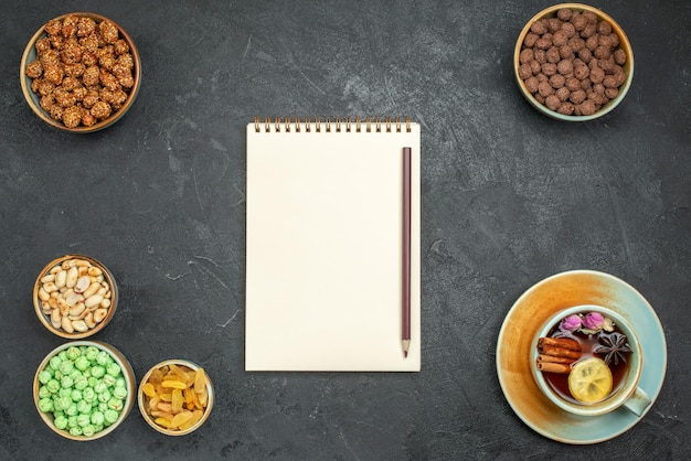 Top view of different sweet candies with nuts and cup of tea on grey