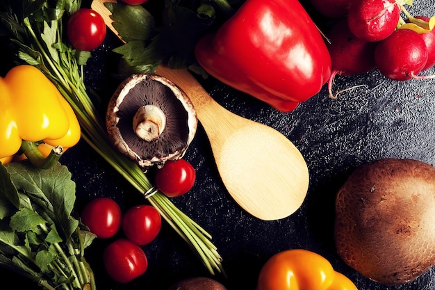 Free photo over top view of different type of vegetables on dark board. red and yellow pepper, mushrooms, cherry and greens