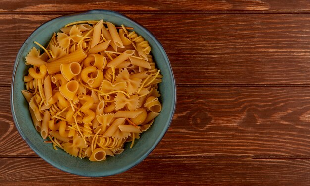 Top view of different types of pasta in bowl on wooden surface with copy space