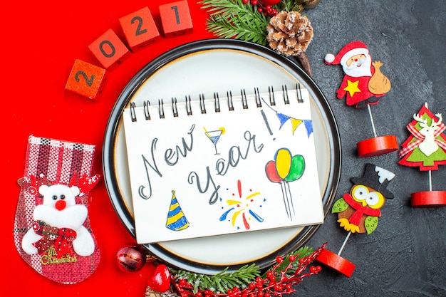 Top view of dinner plate decoration accessories fir branches and numbers christmas sock on a red napkin on a black background