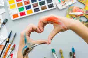 Free photo top view dirty hands making a heart with painting materials