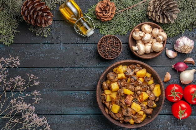 Top view dish and spices plate of mushrooms and potatoes under the bottle of oil bowl of mushrooms and the spruce branches with cones next to garlic onion tomatoes