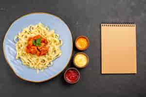 Free photo top view dish with sauces appetizing pasta with gravy and meat in the plate next to the cream notebook three kind of sauces on the dark table