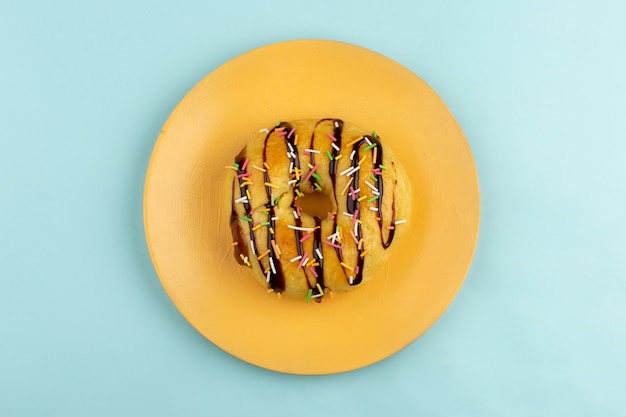 Free photo top view donut with choco lines and colorful candies inside orange plate on the ice-blue floor