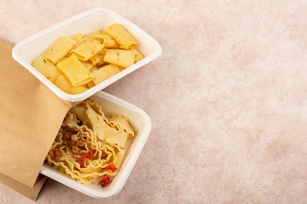 A top view dough meal and italian pasta with tomatoes and meat inside white bowls and package on pink