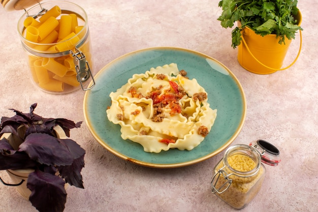 Free photo a top view dough pasta cooked tasty with meat vegetables and salted inside round green plate with flower and raw pasta on pink desk