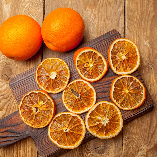 Top view dried orange on cutting board and fresh oranges on wooden table