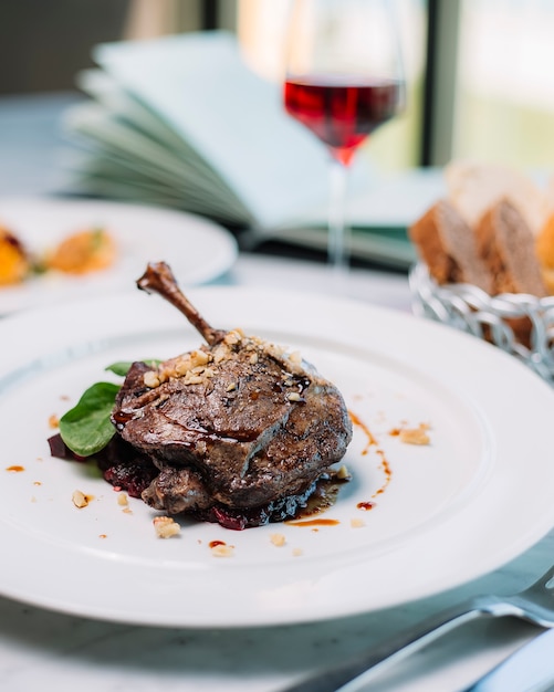 Top view of duck leg cooked in sauce garnished with spinach and walnut