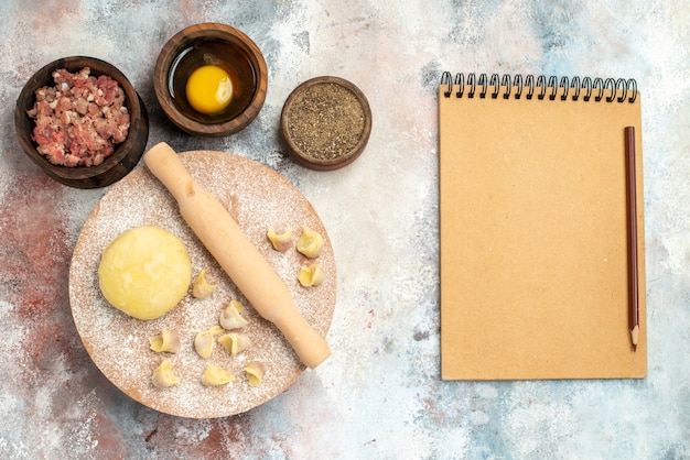 Free Photo top view dushbara dough rolling-pin on dough pastry board bowls with meat pepper egg yolk notebook pencil on nude surface