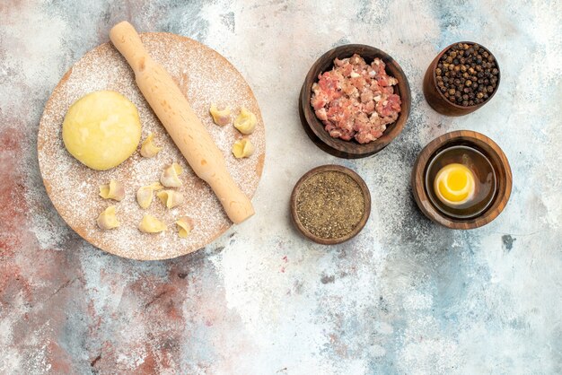 Top view dushbara dough rolling-pin on dough pastry board bowls with meat pepper egg yolk on nude surface with copy space