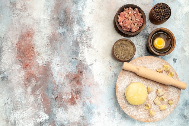 Free Photo top view dushbara dough rolling-pin on dough pastry board bowls with meat pepper egg yolk on nude surface with free place