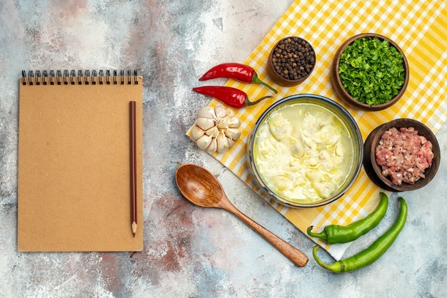 Free photo top view dushbara dumplings soup in a bowl garlic hot peppers wooden spoon bowls with meat pepper and greens a notebook on nude table