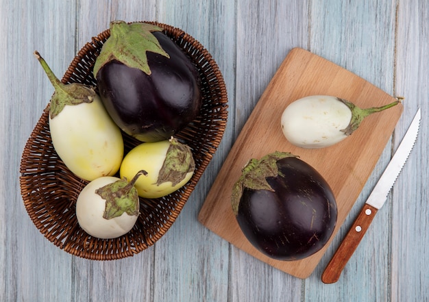 Free photo top view of eggplants in basket and on cutting board with knife on wooden background