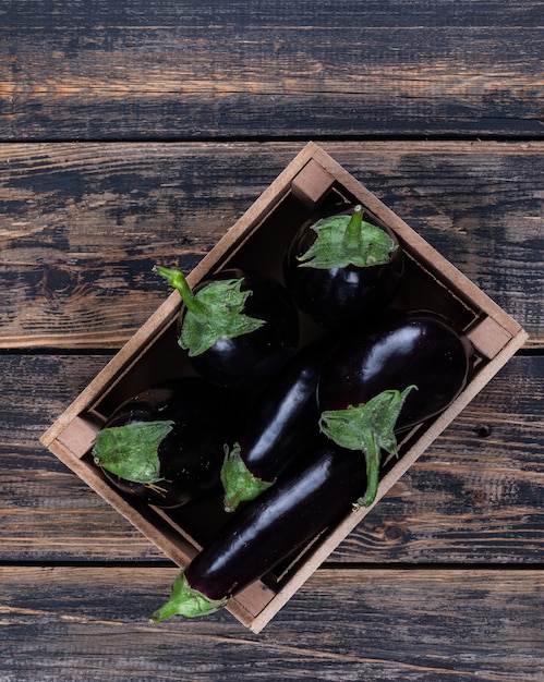 Free photo top view eggplants in wooden box on dark wooden background. vertical