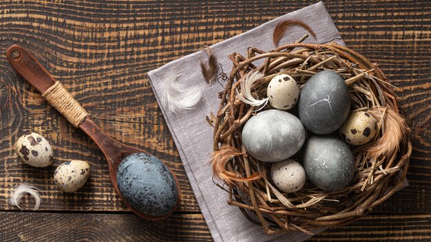 Top view of eggs for easter in twigs nest with wooden spoon and feathers