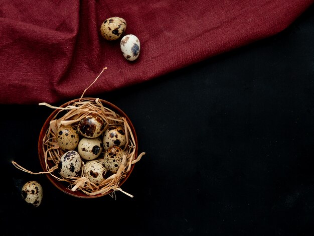 Top view of eggs with nest in bowl on burgundy and black background with copy space