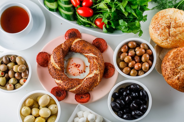 Top view eggs with sausage in plate with a cup of tea, turkish bagel, salad on white surface