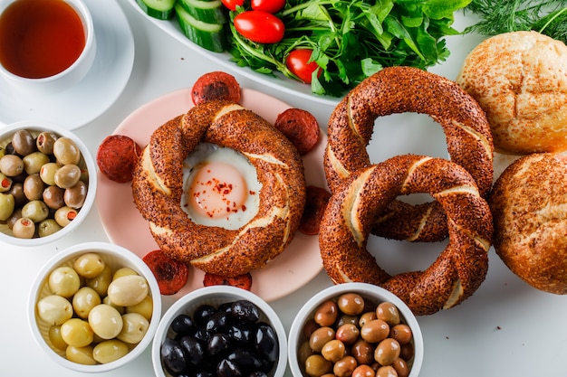 Top view eggs with sausage in plate with a cup of tea, turkish bagel, salad on white surface