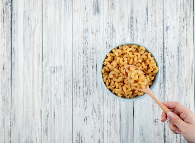 Top view elbow macaroni pasta in bowl on the right with copy space on white wooden background