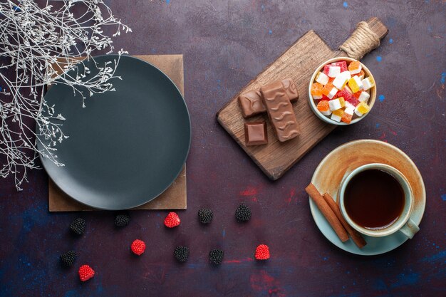 Top view of empty dark plate round formed with tea and candies on the dark surface