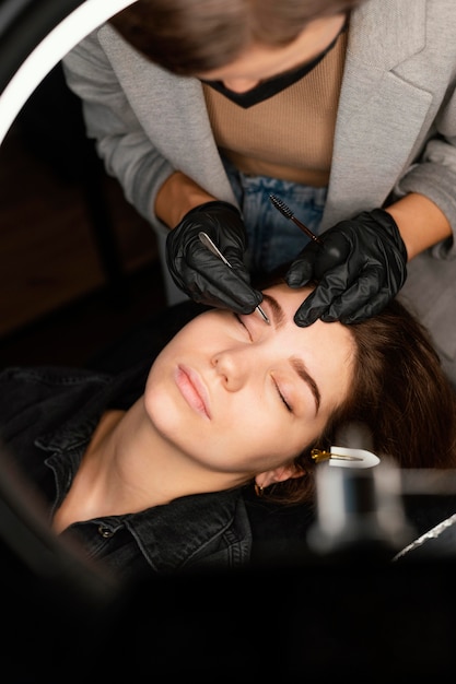 Top view of female clinician doing an eyebrow treatment for woman