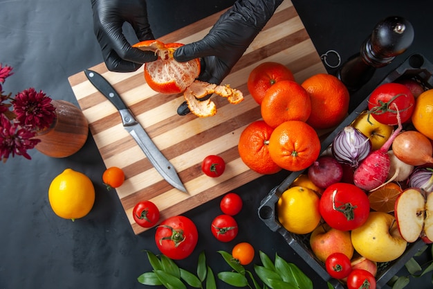 Top view female cook cleaning tangerines on the dark surface