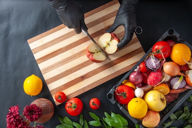 Top view female cook cutting apple on the dark surface