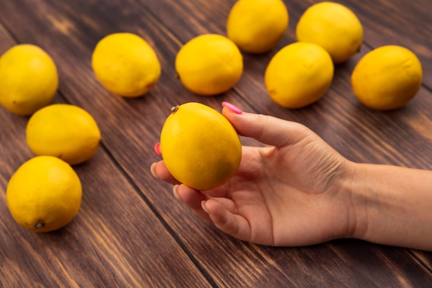 Free Photo top view of female hand holding a fresh lemon on a wooden background