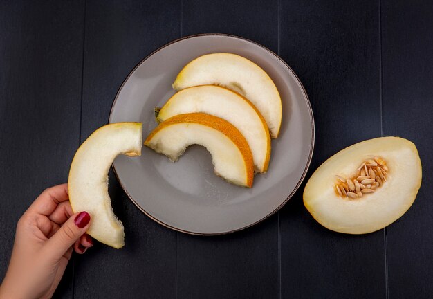 Top view of female hand holding melon slice with slices on plate on wood