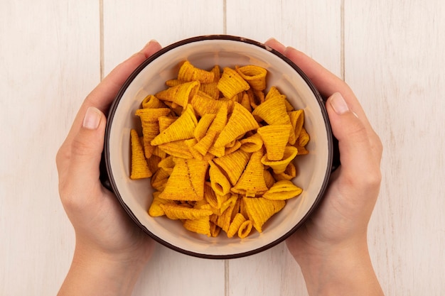 Free photo top view of female hands holding a bowl of crispy tasty chips on a beige wooden table