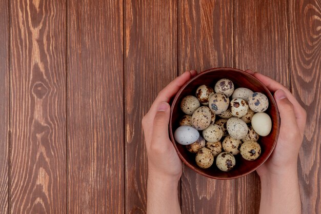 Top view of female hands holding a wooden bowl of quail eggs on a wooden background with copy space