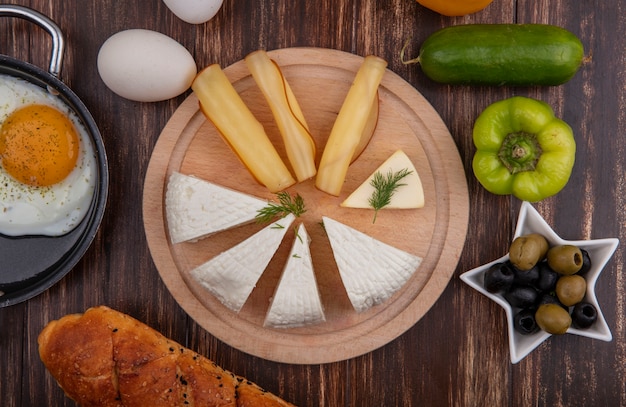 Free Photo top view feta cheese with smoked cheese on a stand with olives  green peppers  cucumber and eggs on a wooden background