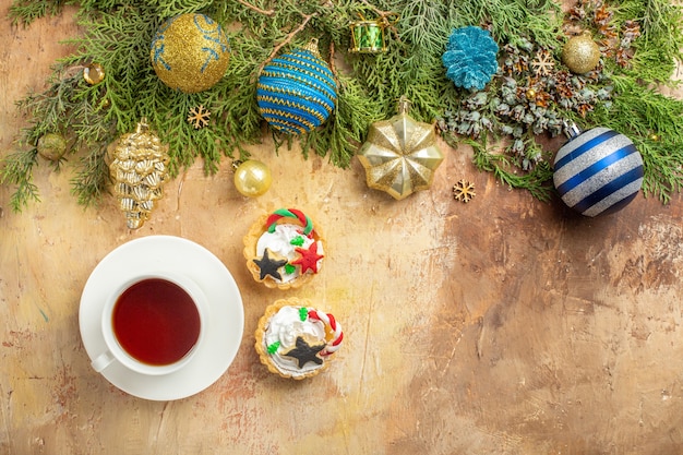 Top view fir branches xmas tree ornaments a cup of tea cupcakes on beige background