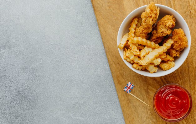 Top view of fish and chips in bowl with ketchup and copy space