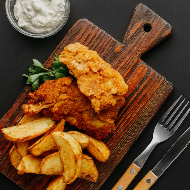 Free photo top view of fish and chips on chopping board with cutlery