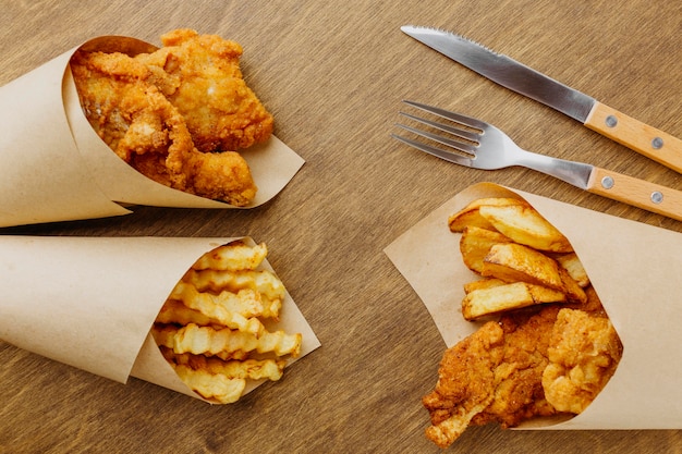 Free photo top view of fish and chips in paper wrap with cutlery