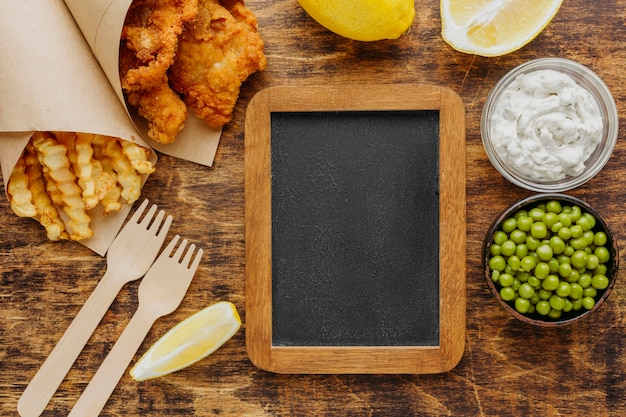 Free Photo top view of fish and chips in paper wrap with peas and chalkboard