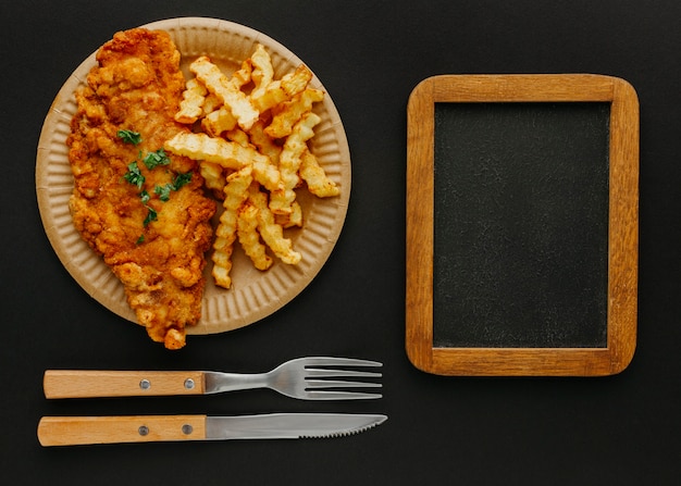 Top view of fish and chips on plate with chalkboard and cutlery