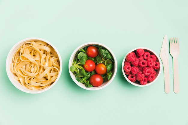 Free photo top view food containers with raspberries, salad and pasta