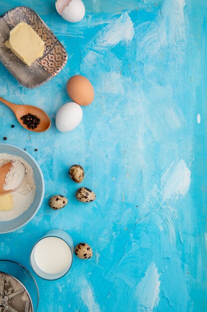 Top view of foods as egg butter flour with milk and black pepper on blue background with copy space