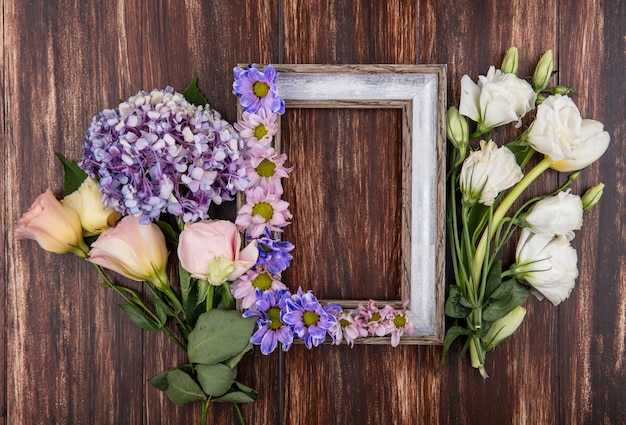 Top view of frame and flowers on it and on wooden background with copy space